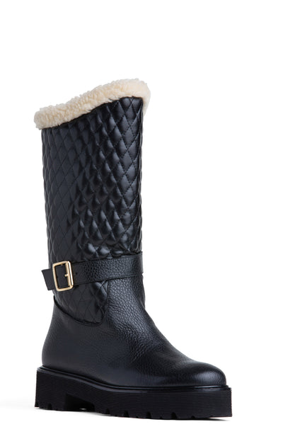 Black leather winter knee-high boot with a faux-fur cuff and a gold-toned buckle on the ankle strap, featuring a quilted pattern on the upper and a rubber lug sole.
