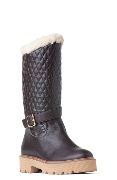 A brown leather winter knee-high boot with a faux-fur cuff and a quilted pattern on the upper portion. It features a gold-toned buckle on the ankle strap and a lug sole.
